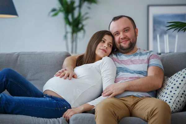快乐的孕妇和男人坐在灰色沙发上的照片 — 图库照片