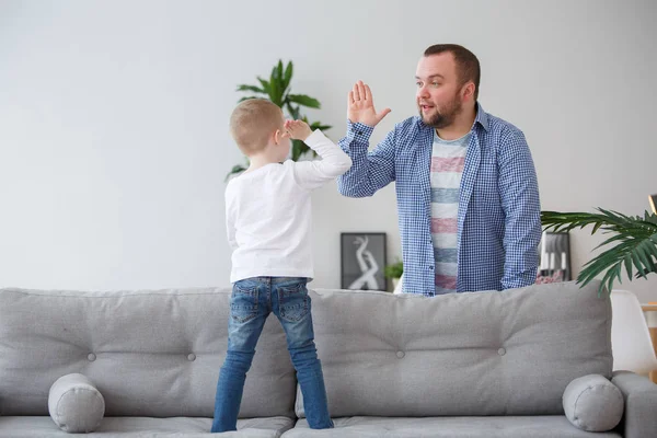 Сімейна фотографія молодого сина, що стоїть на дивані, робить рукостискання з батьком — стокове фото