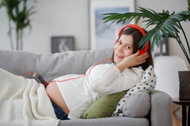 Görüntü hamile kadının koltukta, yalan kulaklık müzik dinlemek