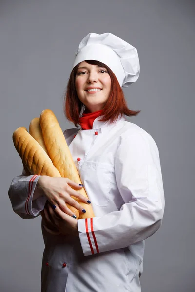 Φωτογραφία της γυναίκα μάγειρας σε λευκό χιτώνα και καπάκι με φραντζόλες — Φωτογραφία Αρχείου