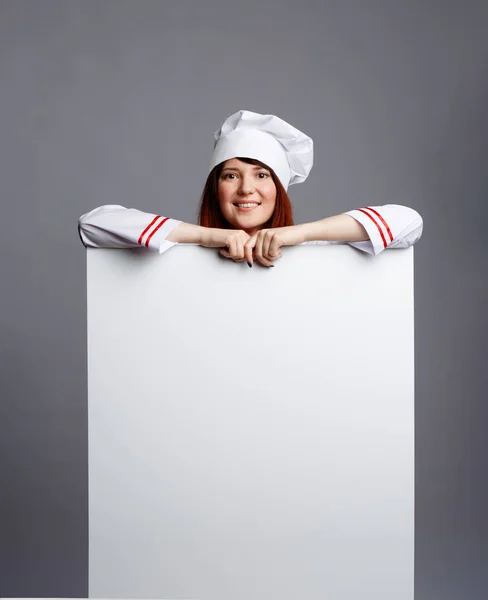 Foto van lachende brunette chef-kok in witte badjas dop met lege papier in handen — Stockfoto