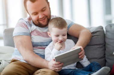 Baba ile oğlu gri koltukta oturan tablet ile görüntü