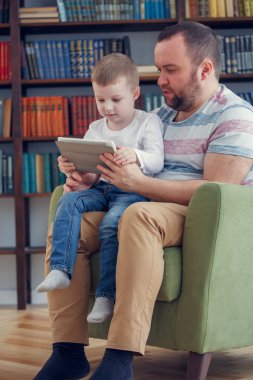Mutlu baba ve genç oğlu ile tablet yeşil sandalye üzerinde oturan resmi