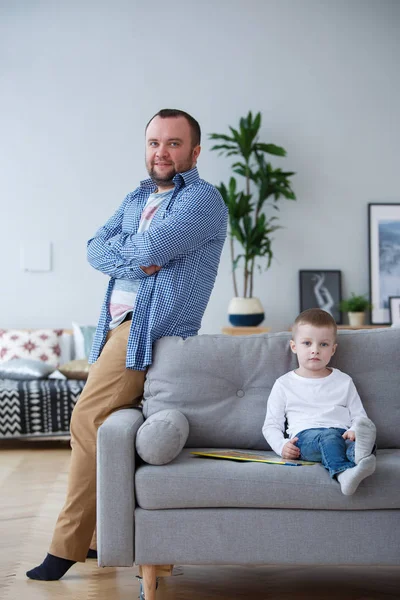 Family photo of father standing at sofa and son sitting on couch — Stock Photo, Image