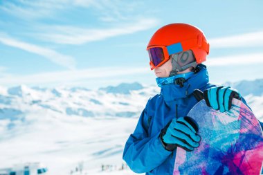 Fotoğraf sportif adamın kask uzakta snowboard ile karlı tepe özgeçmişlerine bakarak.