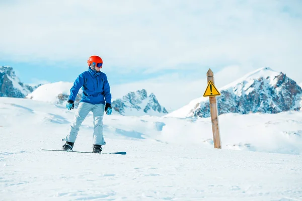 山で警告サインでヘルメット身に着けているスノーボーダーの写真 — ストック写真