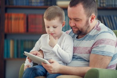 Mutlu baba ve küçük oğlu ile tablet yeşil sandalye üzerinde oturan fotoğrafı