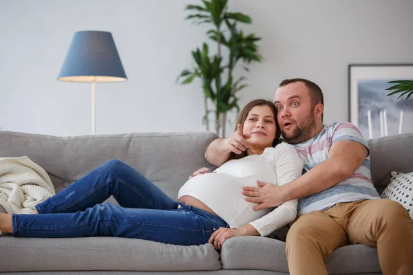 快乐的孕妇和坐在灰色沙发上的男人的形象 — 图库照片
