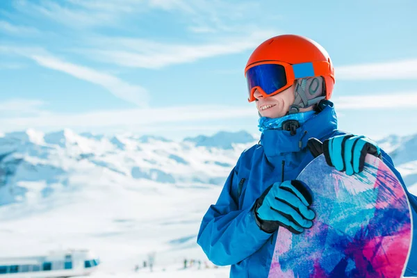 雪に覆われた丘の背景にスノーボード、ヘルメットがよそ見でスポーティな男のイメージ — ストック写真