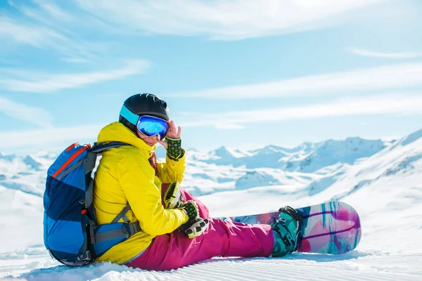 Foto van vrouw in helm met rugzak zittend op sneeuw met snowboard — Stockfoto