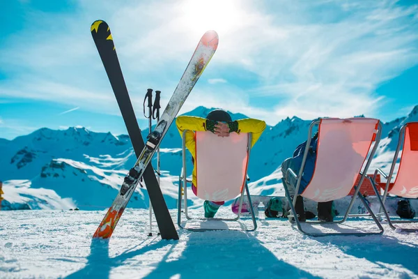 Photo from back of vacationers in armchair, skis, sticks in snowy resort — Stock Photo, Image