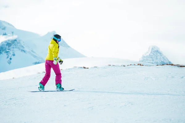 Foto de la espalda de una mujer joven en el casco de snowboard en la montaña nevada — Foto de Stock