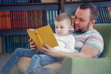 Sandalyede oturan oğlu kitap okuma baba fotoğrafı