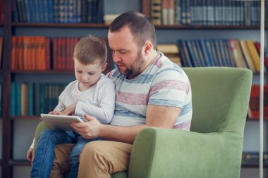 Mutlu baba ve genç oğlu ile tablet yeşil sandalye üzerinde oturan görüntü