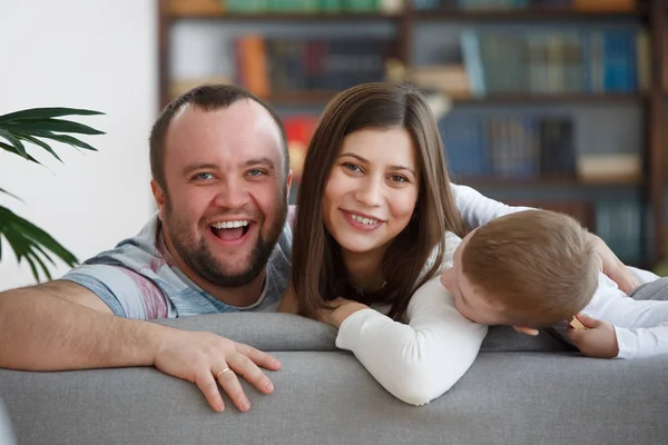 Imagen de la familia sonriente con su hijo sentado en un sofá gris — Foto de Stock
