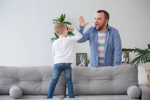 Family picture of young son standing on couch doing handshake with dad