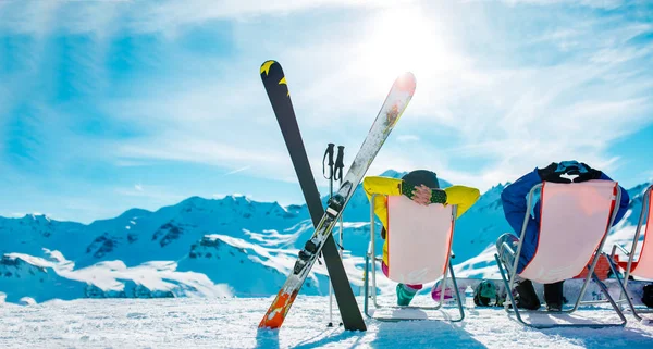 Image from back of vacationers in armchair, skis, sticks in snowy resort — Stock Photo, Image