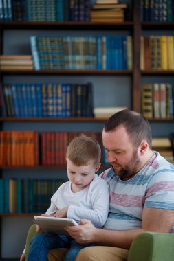 Baba ve küçük oğlu ile tablet yeşil sandalye üzerinde oturan aile fotoğrafı