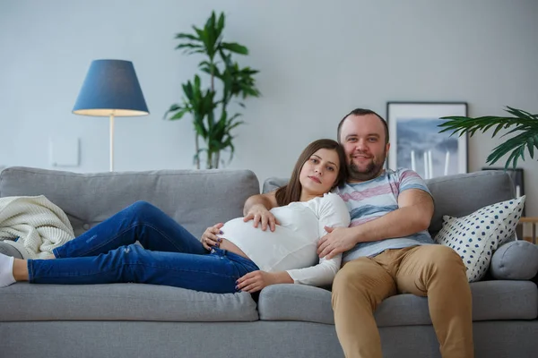 Εικόνα ευτυχισμένη έγκυος γυναίκα και άνδρα σε γκρι καναπέ — Φωτογραφία Αρχείου