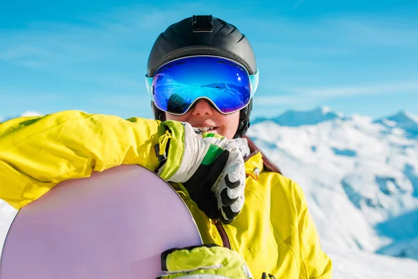 Retrato de morena sorridente no capacete e máscara com snowboard no fundo de colinas nevadas — Fotografia de Stock