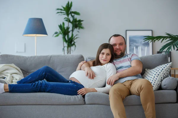 Zdjęcie szczęśliwej kobiety w ciąży i mężczyzny na szarej sofie — Zdjęcie stockowe