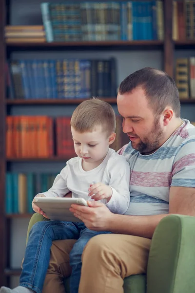 Imagem familiar de pai e pequeno filho sentado com tablet na cadeira verde — Fotografia de Stock