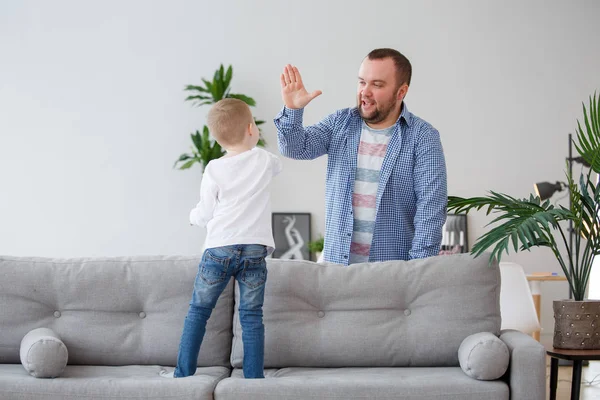 Familienbild des kleinen Sohnes, der auf dem Sofa steht und mit Papa den Händedruck macht — Stockfoto