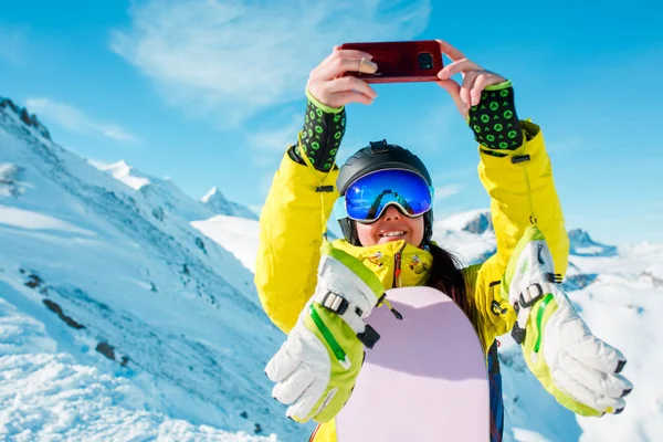 Imagem de mulher de esportes usando capacete fazendo selfie contra o fundo de colinas nevadas — Fotografia de Stock