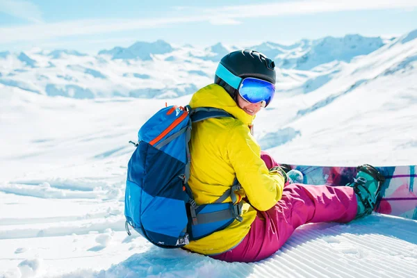 Gelen kadın kask içinde arkasında kar snowboard ile oturup sırt çantası ile resim — Stok fotoğraf