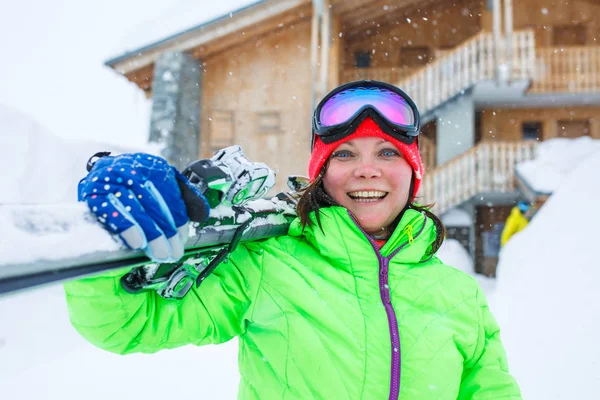 Vrouw in helm met ski's op schouder op achtergrond van houten gebouw — Stockfoto