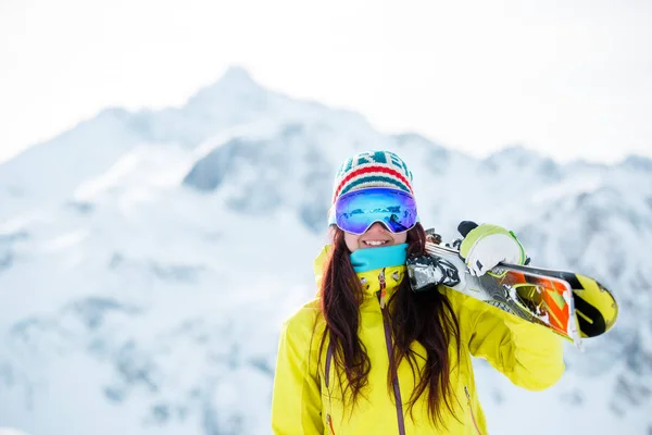 Foto van vrouw in masker met ski's op haar schouder tegen een achtergrond van besneeuwde heuvel — Stockfoto