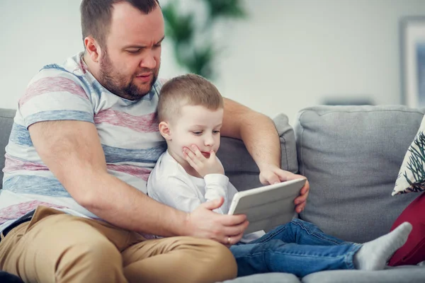 Foto di padre con figlio con tablet seduto sul divano grigio — Foto Stock