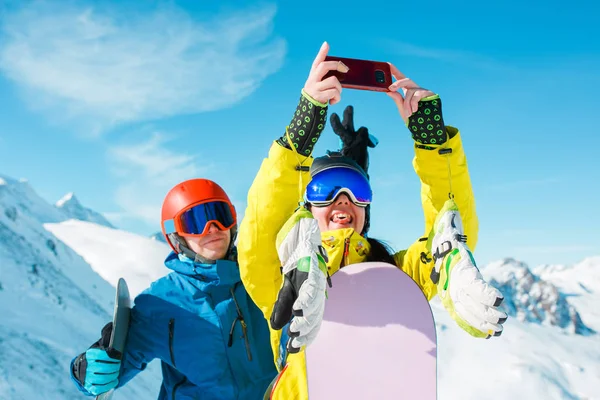 Imagem de homem e mulher de esportes no capacete fazendo selfie contra o fundo de colinas nevadas — Fotografia de Stock