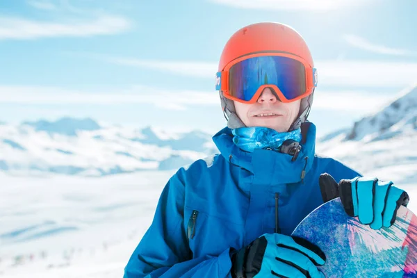 Portrét sportive člověka v helmě, při pohledu na fotoaparát s snowboard na pozadí zasněženého kopce — Stock fotografie