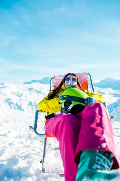 Pictures of sporty woman with helmet resting on chair in winter resort — Stock Photo, Image