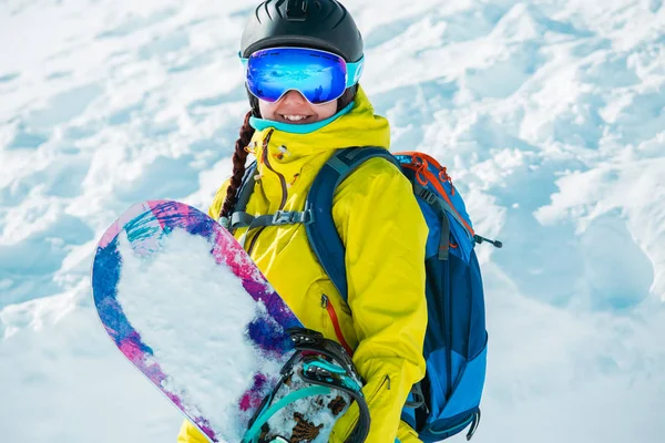 Photo de femme souriante en casque et avec snowboard en fond de paysage enneigé — Photo