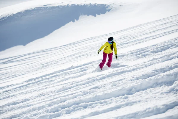 Foto de morena con casco y máscara en ropa deportiva, snowboard desde la ladera nevada de la montaña —  Fotos de Stock