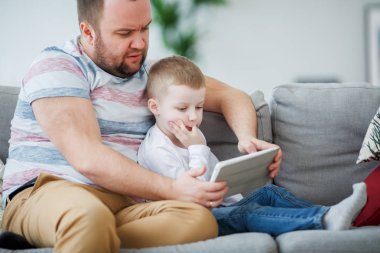 Bir baba ile oğlu gri koltukta oturan tablet ile görüntü