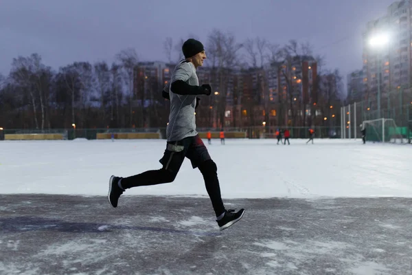 Foto eines Mannes in schwarzer Sportkleidung, der entlang des Winterparks vor Häuserhintergrund läuft — Stockfoto