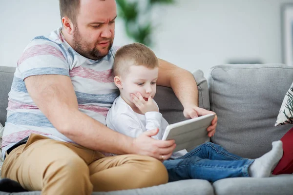 父亲的形象与儿子坐在灰色沙发上的平板电脑 — 图库照片