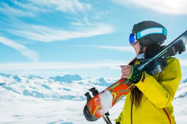 Photo de la vue latérale de la femme sportive en casque avec des skis sur son épaule sur fond de collines hivernales — Photo