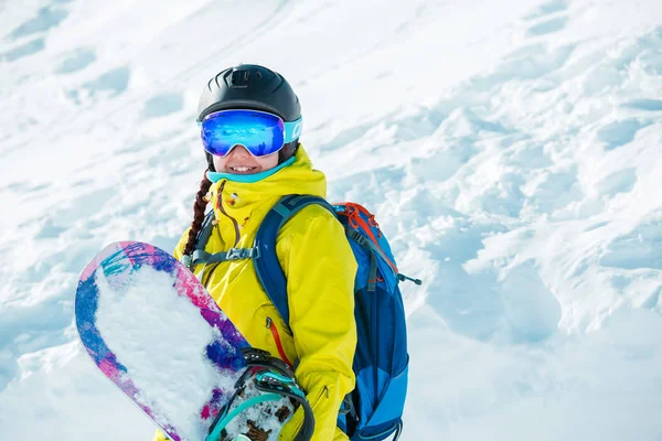 Foto de mujer sonriente en casco y con snowboard sobre fondo de paisaje nevado —  Fotos de Stock