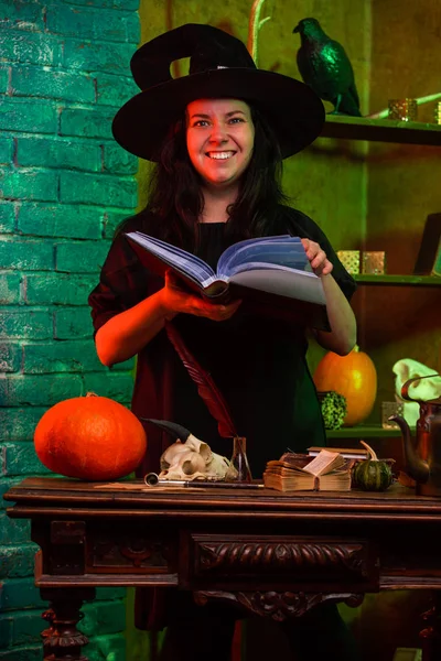 Retrato de bruja con libro en la mesa con calabaza, cráneo —  Fotos de Stock