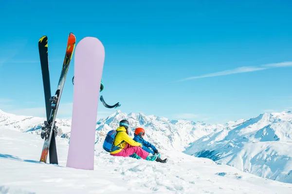 Foto de snowboard, esquís en el fondo de la pareja de deportes sentado en la colina nevada — Foto de Stock
