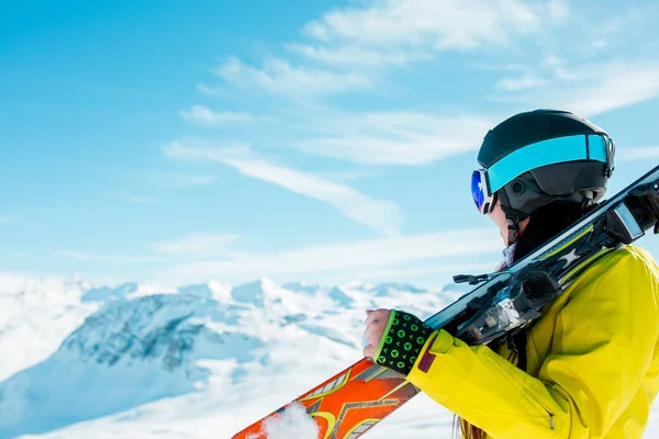 Side view of sporty woman in helmet with skis on her shoulder against background of winter hills — Stock Photo, Image
