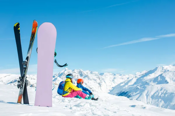 Imagen de snowboard, esquí en el fondo de la pareja de deportes sentado en la colina nevada en la tarde de invierno — Foto de Stock