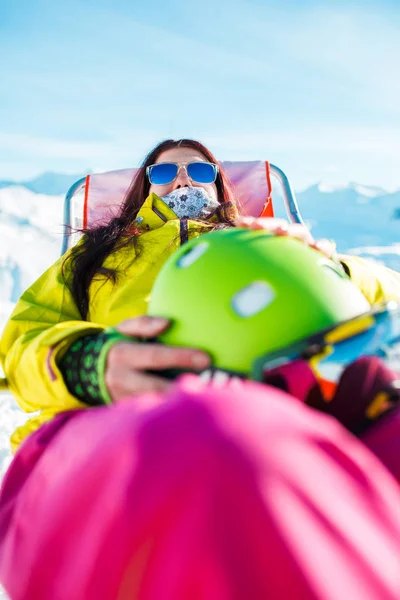 Portrait of sports long-haired brunette with helmet resting on chair in winter resort — Stock Photo, Image