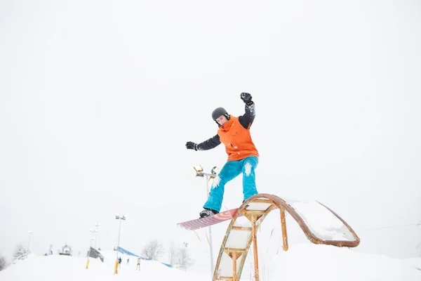 Bild eines jungen sportlichen Mannes, der auf einem Snowboard mit Sprungbrett gegen den verschneiten Himmel fährt — Stockfoto