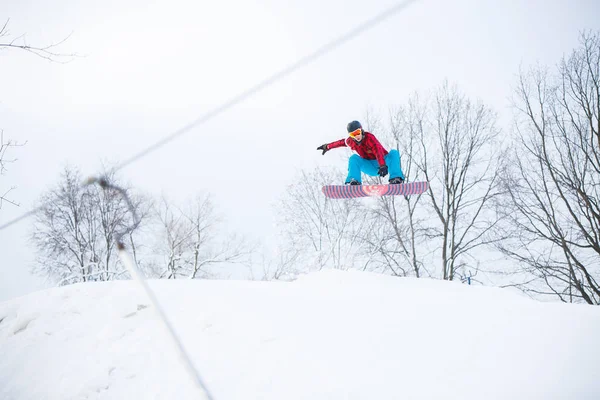 Imagem do snowboarder masculino esportivo que salta na colina nevada — Fotografia de Stock