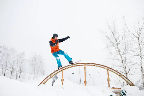 Foto do jovem homem esportivo esquiando em snowboard com trampolim contra fundo de árvores — Fotografia de Stock